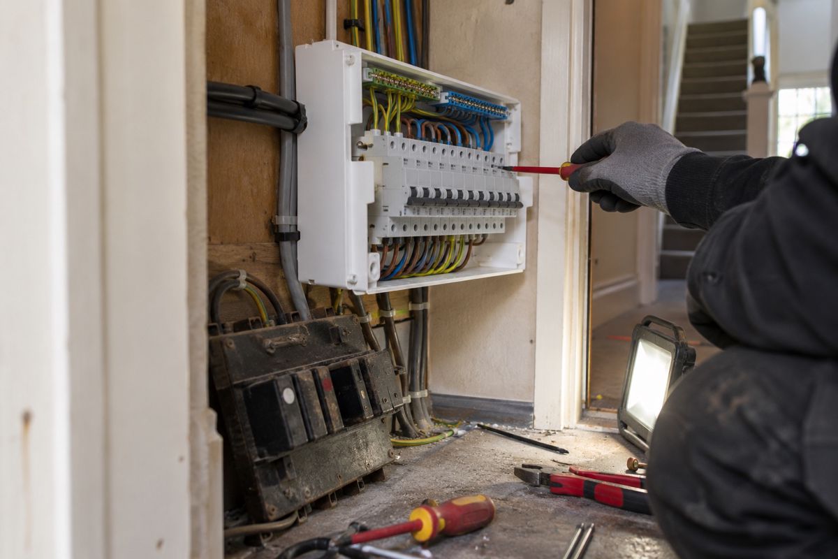 New consumer unit being fitted beside an old fuse board in a hallway cupboard